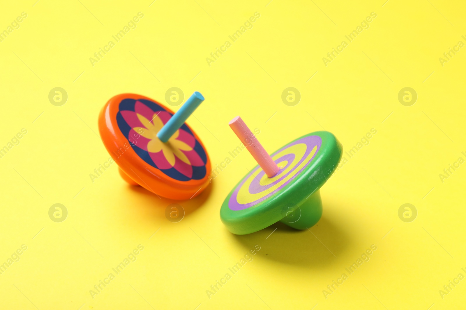 Photo of Two colorful spinning tops on yellow background, closeup