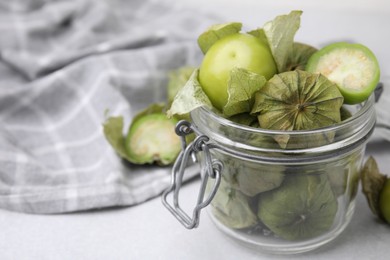 Photo of Fresh green tomatillos with husk in glass jar on light table, closeup