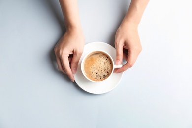 Photo of Young woman with cup of delicious hot coffee on light background, top view