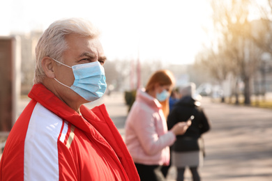 Senior man with medical mask on city street. Virus protection