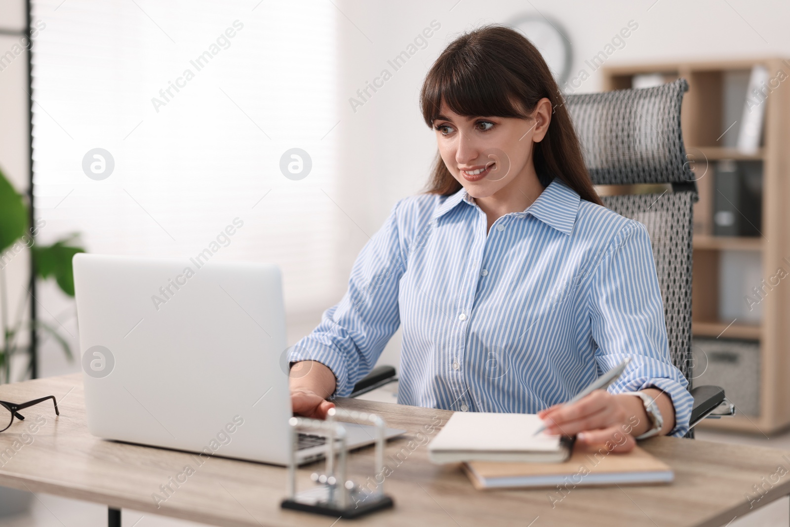 Photo of Woman taking notes during webinar at wooden table indoors