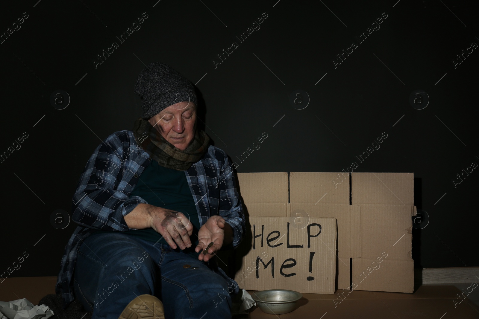 Photo of Poor senior man counting coins near cardboard sign HELP ME and dark wall. Space for text