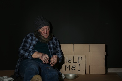 Poor senior man counting coins near cardboard sign HELP ME and dark wall. Space for text