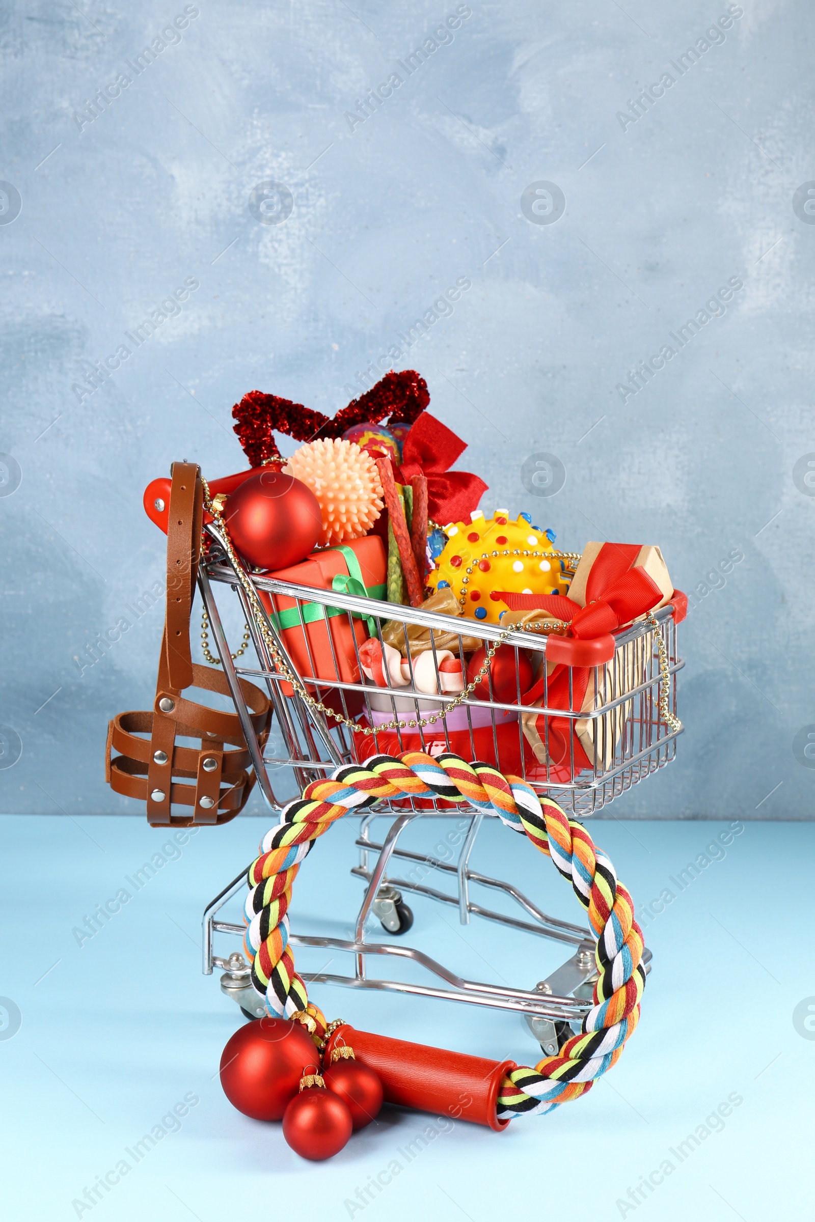 Photo of Small shopping cart with different pet goods and Christmas gifts on light blue background. Shop assortment