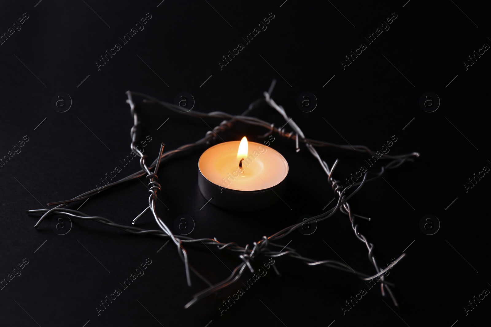 Photo of Burning candle and star of David made with barbed wire on black background. Holocaust memory day