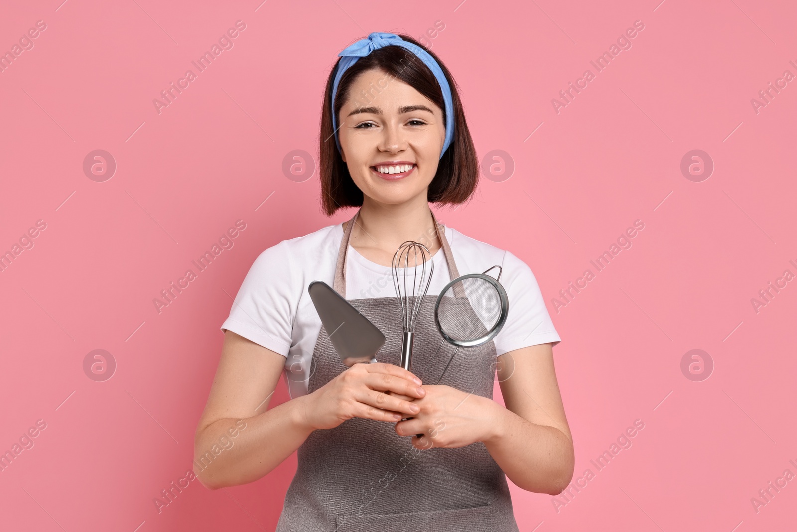 Photo of Happy confectioner with professional tools on pink background