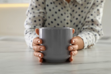 Woman with grey cup at table indoors, closeup