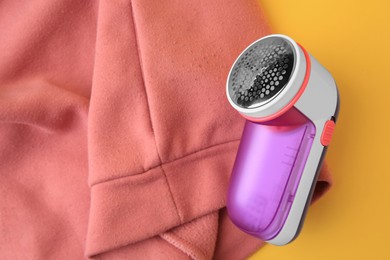 Photo of Modern fabric shaver and pink sweater with lint on yellow background, top view