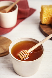 Jar of fresh honey and dipper on white wooden table