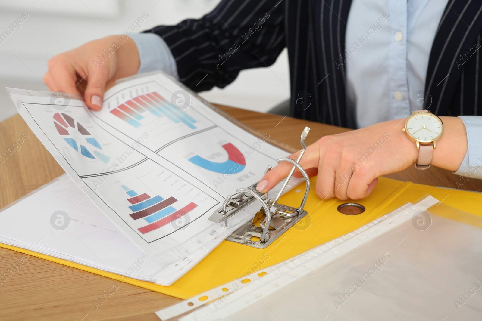 Photo of Businesswoman putting document into file folder at wooden table in office, closeup