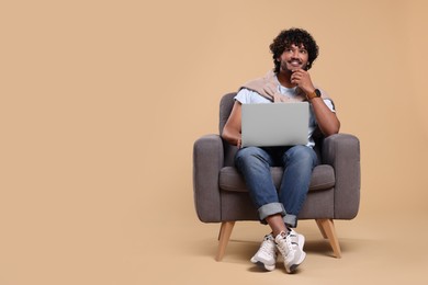Photo of Smiling man with laptop sitting in armchair on beige background, space for text