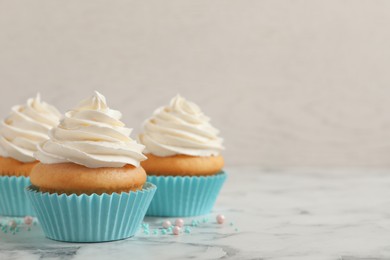 Photo of Delicious cupcakes decorated with cream on white marble table, space for text