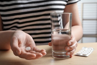 Woman with glass of water and pill at wooden table, closeup