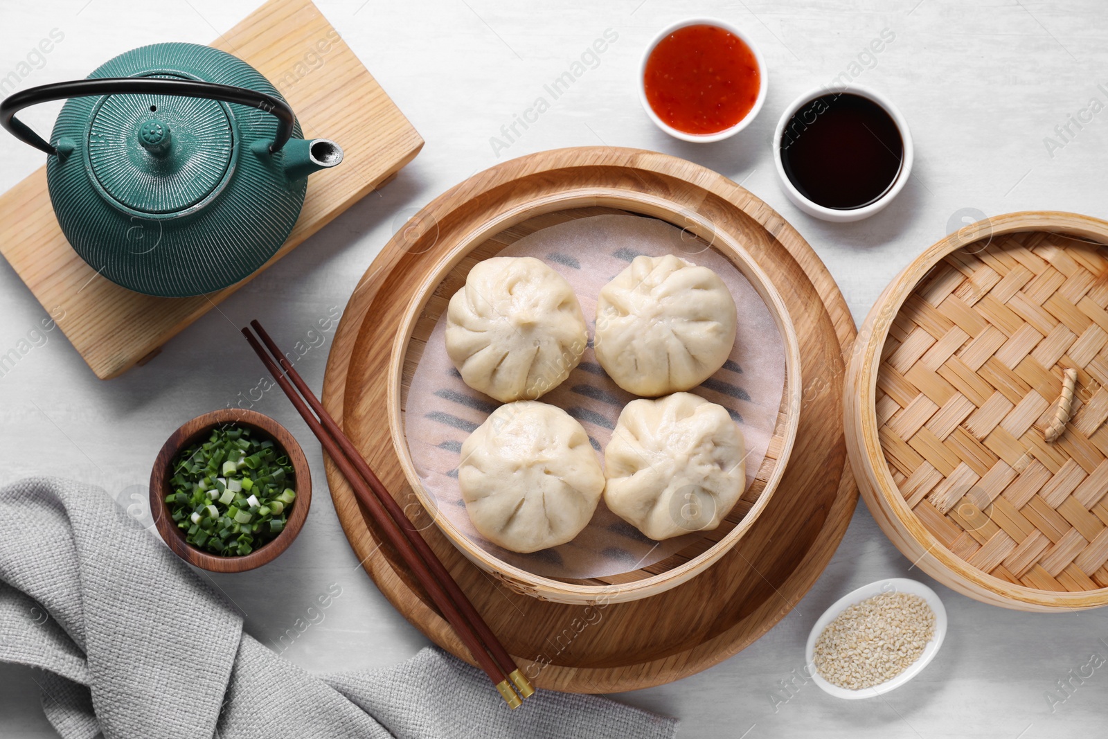 Photo of Delicious bao buns (baozi), chopsticks, sauces, seasonings and kettle on light table, flat lay