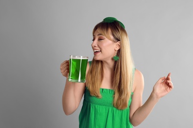 Woman in St Patrick's Day outfit drinking beer on light grey background