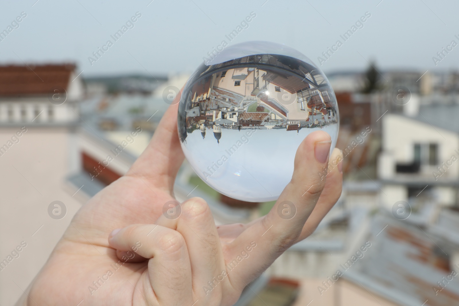 Photo of View of beautiful city street, overturned reflection. Man holding crystal ball outdoors, closeup