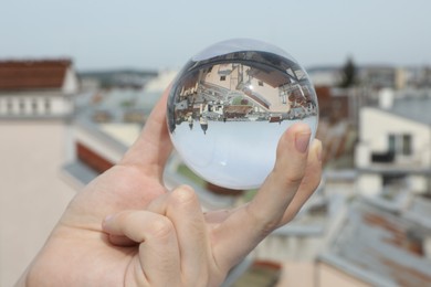 View of beautiful city street, overturned reflection. Man holding crystal ball outdoors, closeup