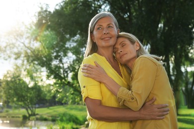 Photo of Family portrait of happy mother and daughter hugging in park on sunny day. Space for text