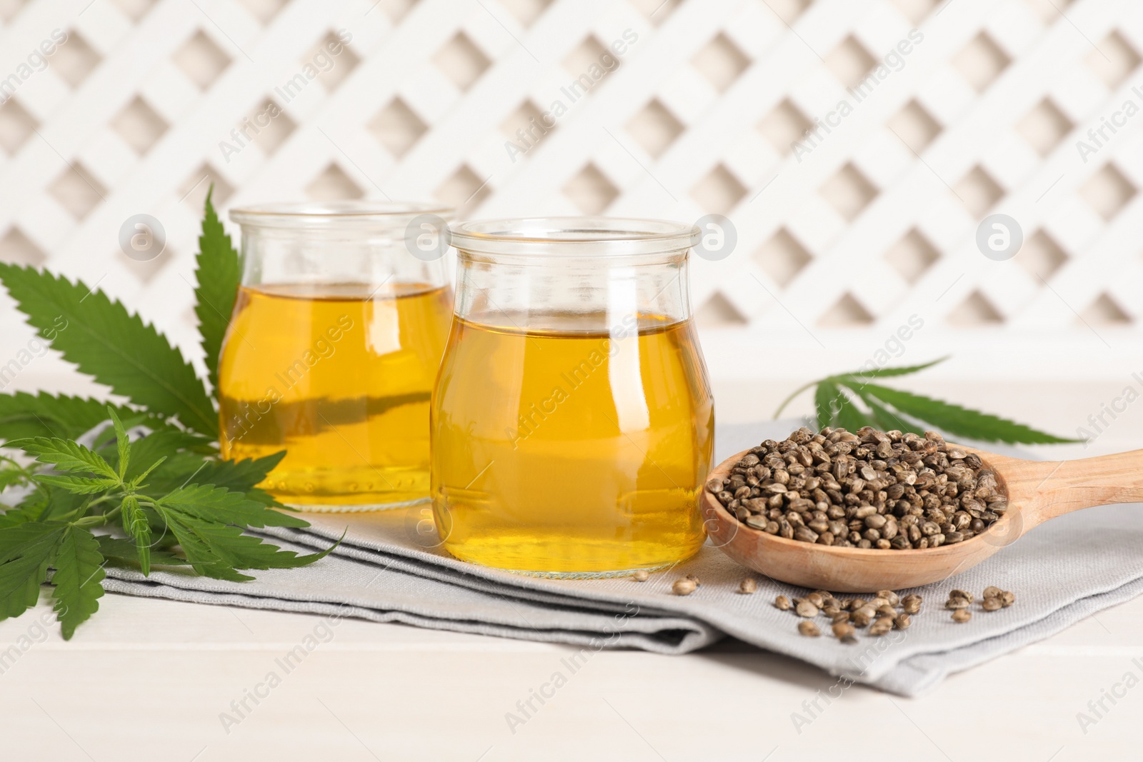 Photo of Hemp oil, fresh leaves and seeds on white wooden table