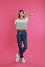 Photo of Young woman with modern laptop on pink background