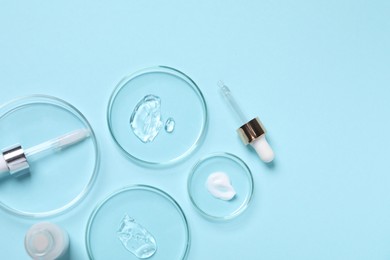 Photo of Petri dishes with samples of cosmetic serums, bottle and pipettes on light blue background, flat lay. Space for text