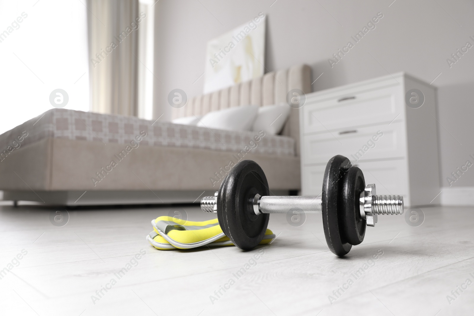 Photo of Steel dumbbell and ankle weights on floor indoors. Fitness at home