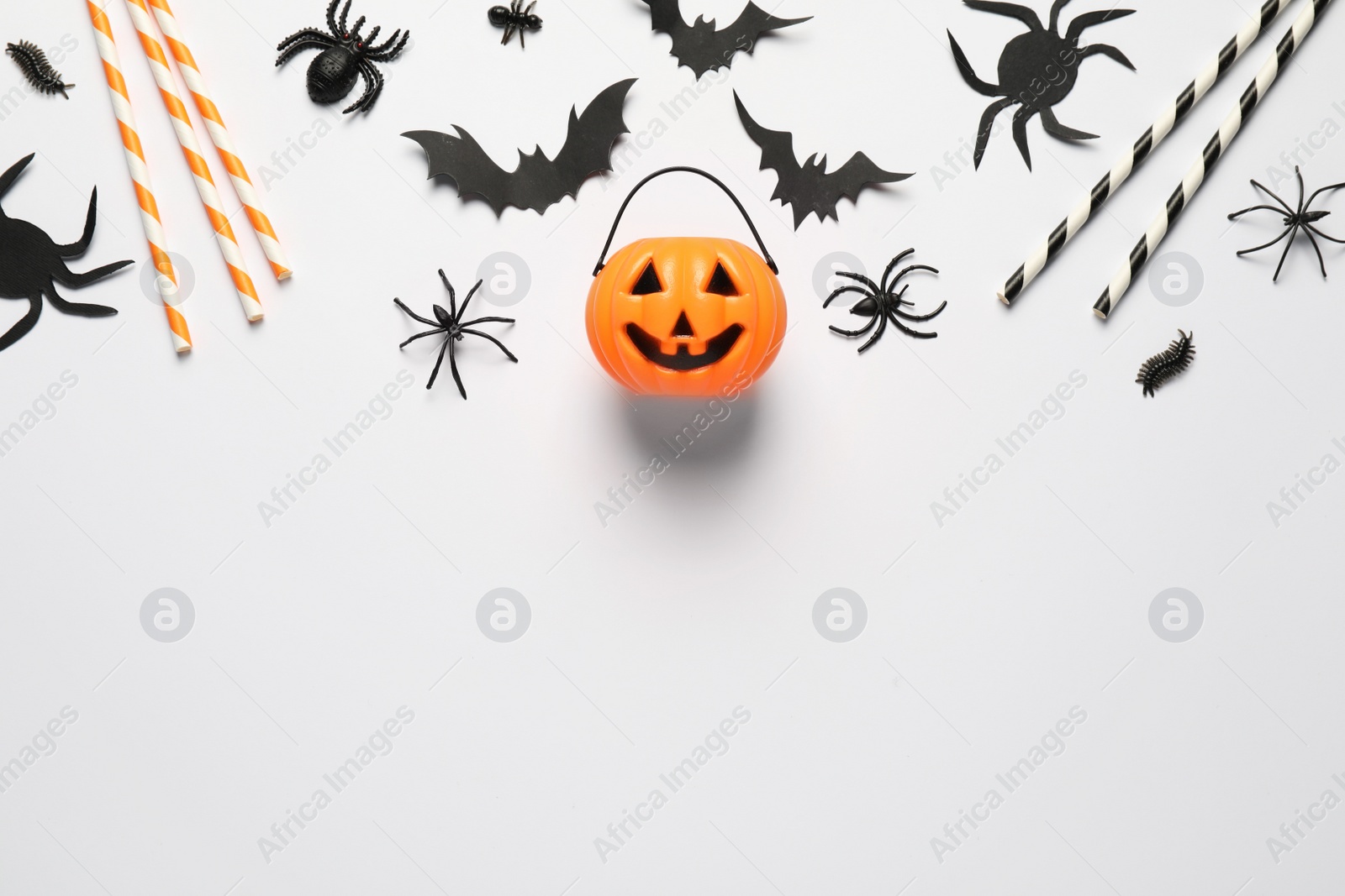 Photo of Flat lay composition with plastic pumpkin basket and paper bats on white background, space for text. Halloween celebration