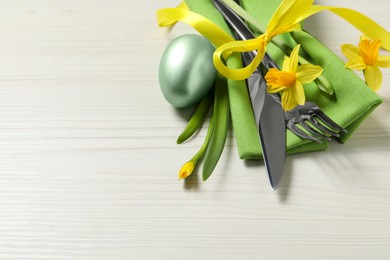 Cutlery set, painted egg and beautiful flowers on wooden table, space for text. Easter celebration