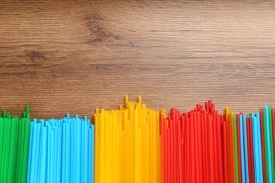 Colorful plastic drinking straws on wooden table, flat lay. Space for text