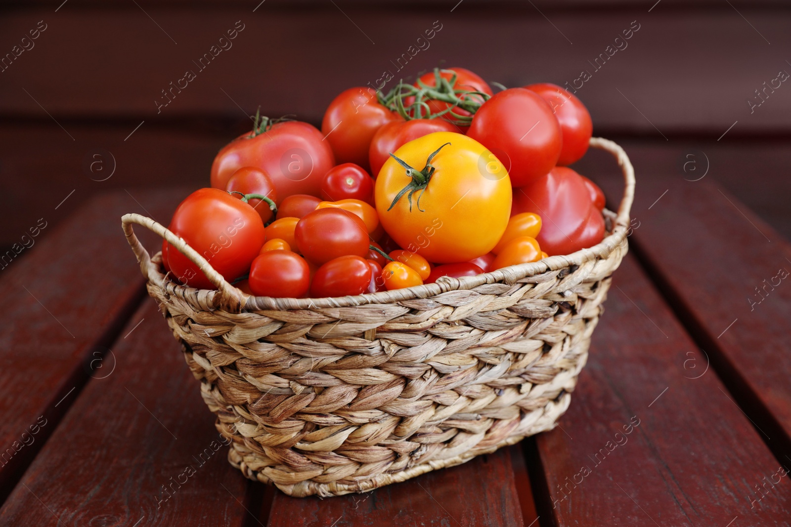 Photo of Wicker basket with fresh tomatoes on wooden table