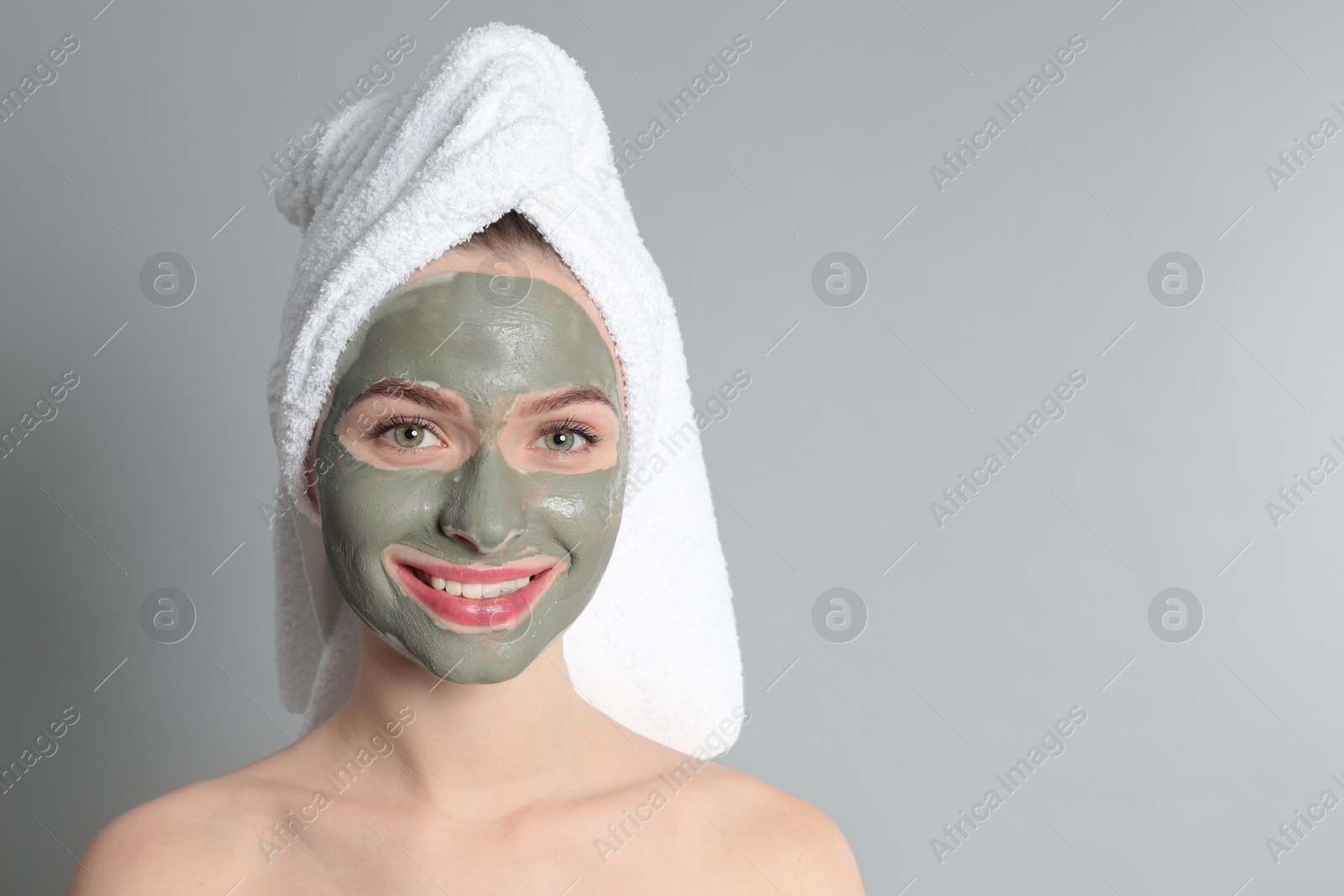 Photo of Young woman with clay mask on her face against grey background, space for text. Skin care