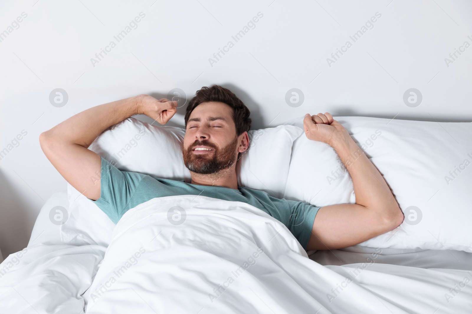 Photo of Happy man stretching on comfortable pillows in bed at home
