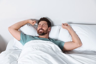 Photo of Happy man stretching on comfortable pillows in bed at home