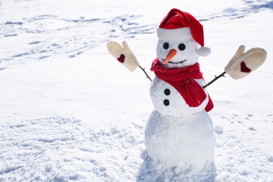Photo of Funny snowman with Santa hat, scarf and mittens outdoors on sunny day. Space for text