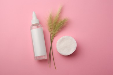 Bottle of makeup remover, cotton pads and spikelets on pink background, flat lay