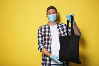 Photo of Male volunteer in protective mask and gloves with black bag on yellow background. Aid during coronavirus quarantine