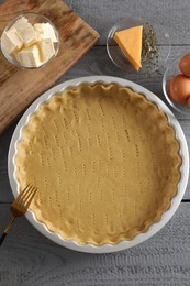 Making quiche. Baking dish with fresh dough and ingredients on grey wooden table, flat lay