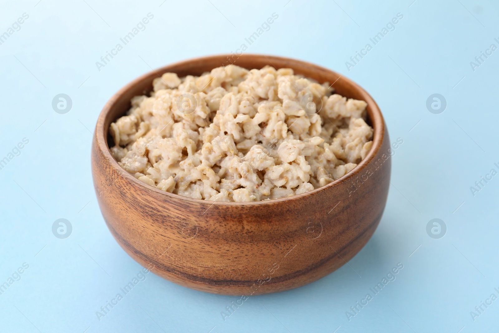 Photo of Tasty boiled oatmeal in bowl on light blue background, closeup