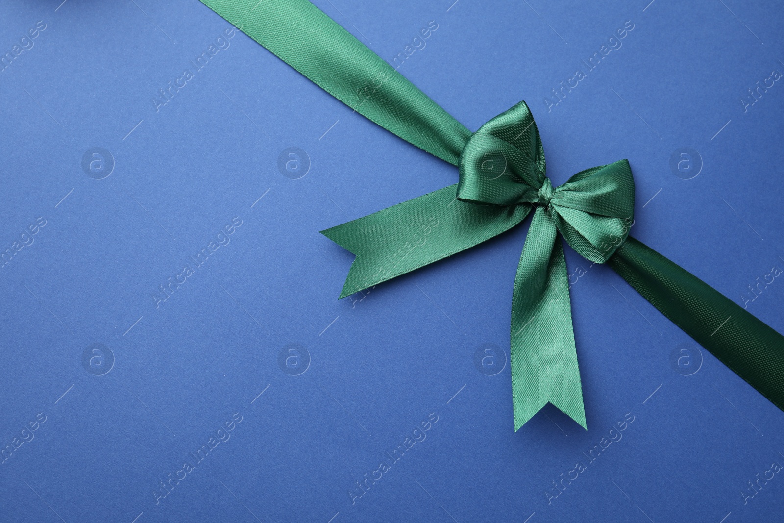 Photo of Green satin ribbon with bow on blue background, top view. Space for text