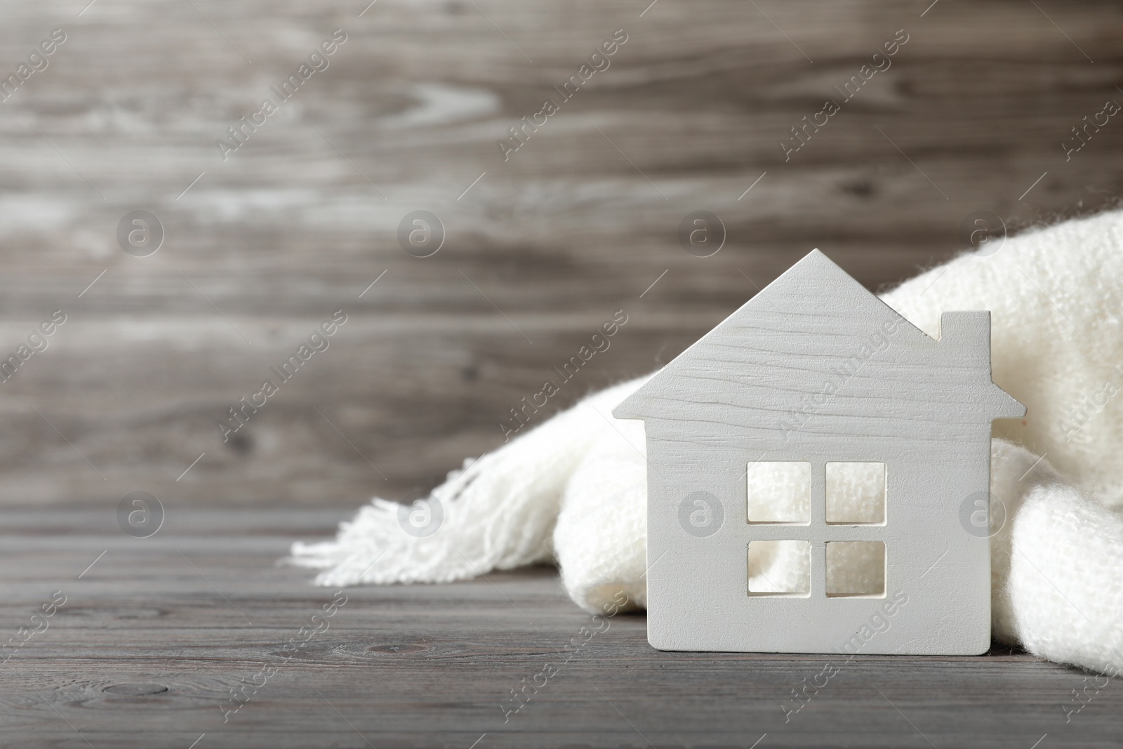 Photo of White house model and scarf on wooden table, space for text. Heating efficiency