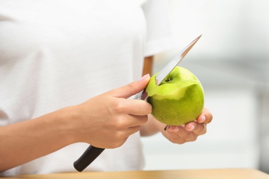 Photo of Woman peeling fresh green apple indoors, closeup view