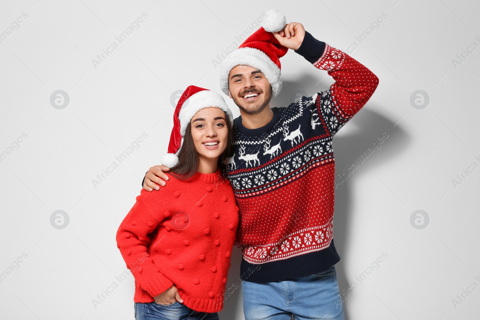Photo of Young couple in warm sweaters and Christmas hats on white background
