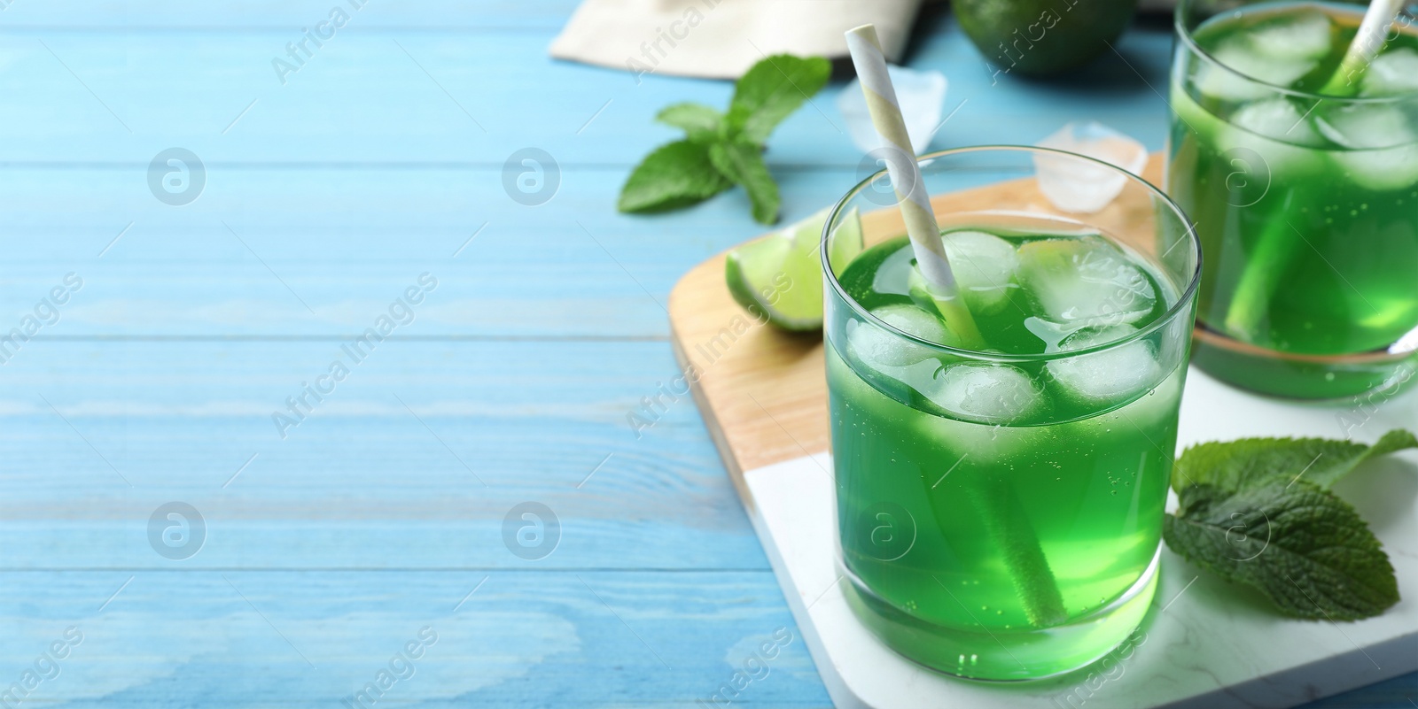 Image of Delicious mint liqueur with green leaves and ice cubes on turquoise wooden table, closeup with space for text. Banner design