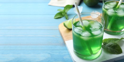 Image of Delicious mint liqueur with green leaves and ice cubes on turquoise wooden table, closeup with space for text. Banner design