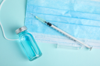 Photo of Vial, syringe and surgical mask on turquoise  background, flat lay. Vaccination and immunization
