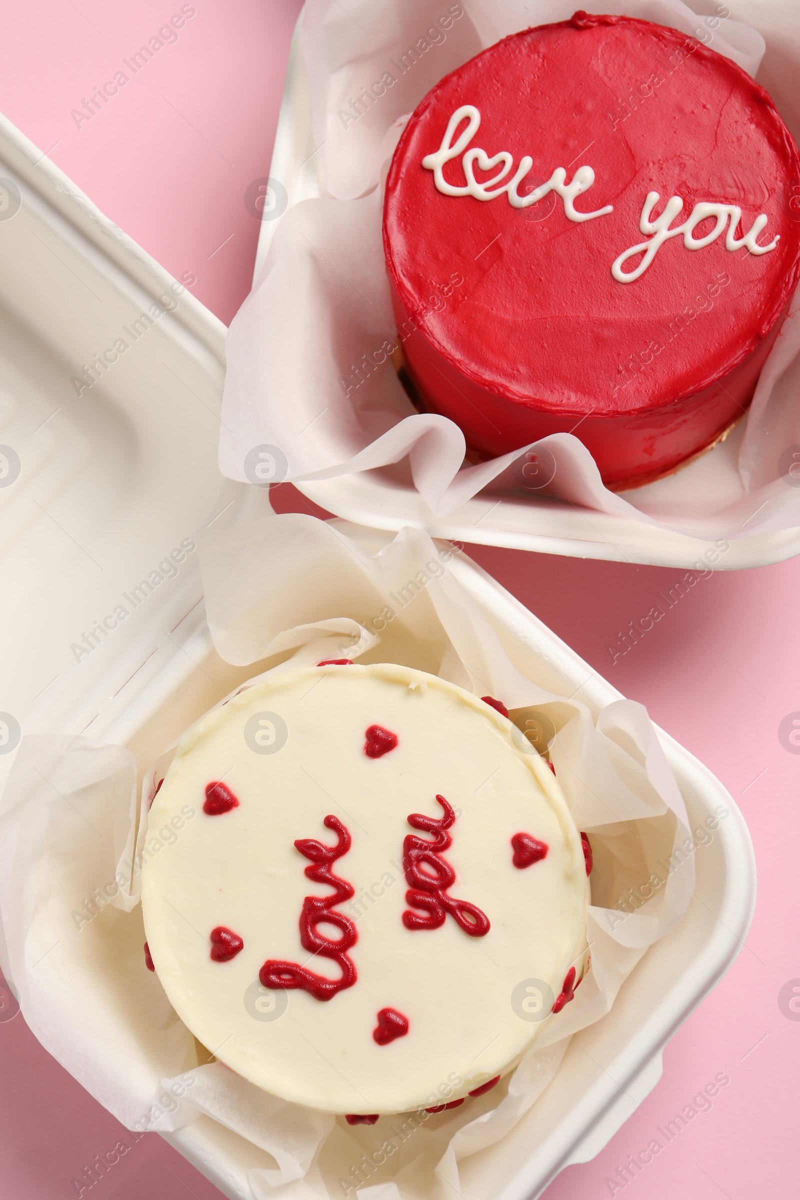 Photo of Bento cakes in takeaway boxes on pink table, flat lay. St. Valentine's day surprise