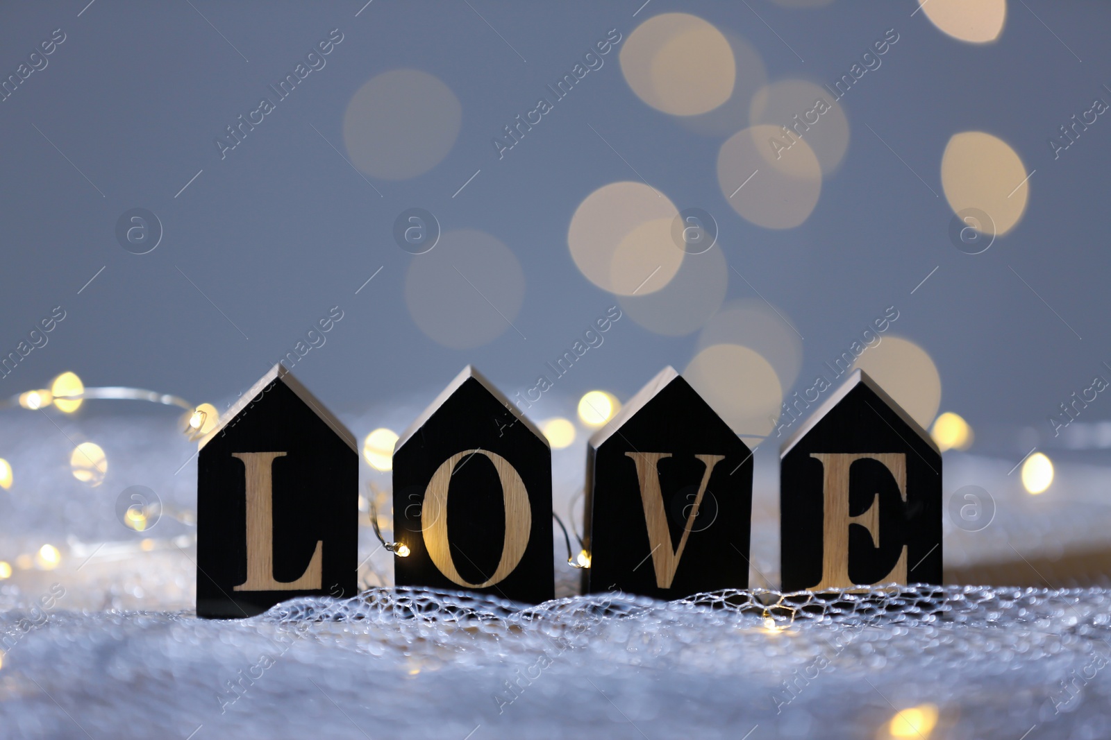 Photo of Word LOVE of wooden letters on mesh fabric against blurred lights. Bokeh effect