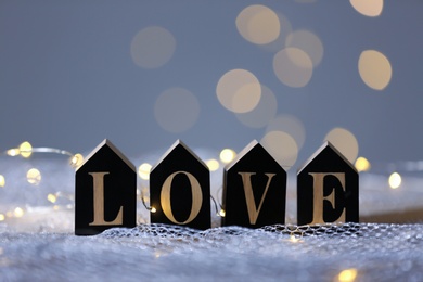 Photo of Word LOVE of wooden letters on mesh fabric against blurred lights. Bokeh effect