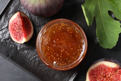 Photo of Jar of tasty fig jam and fresh fruits on black table, flat lay