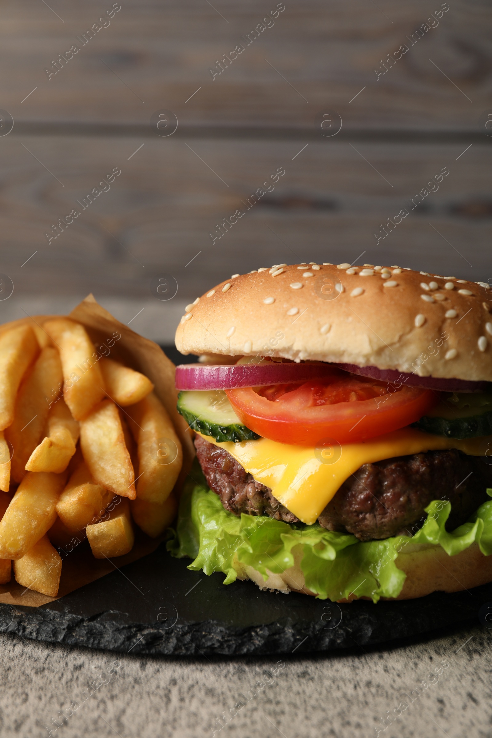 Photo of Delicious burger and french fries served on grey table, closeup